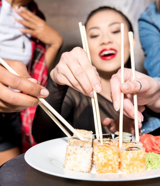 selective focus of asian woman eating sushi with friends